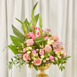 Pink roses and mixed blooms arranged in a gold pedestal vase