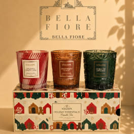 Three scented candles in decorative glass holders on a holiday gift box
