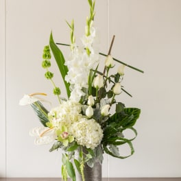 Tall white floral arrangement in a silver vase with candles beside it