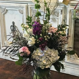 Tall mixed flower arrangement in a glass vase with purple, white, and pink blooms