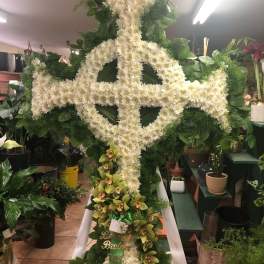 Large white floral cross on an easel with green orchids at the base