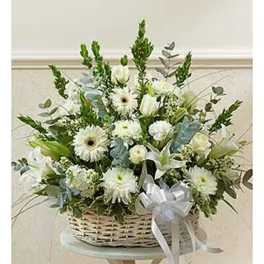 White floral arrangement in a wicker basket with a ribbon bow