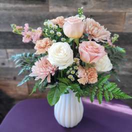 Arrangement of pale pink and white roses, carnations, and mums in a white vase