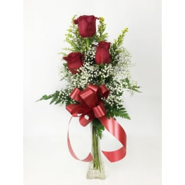 Three red roses in a clear vase with baby's breath and a red ribbon