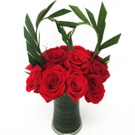 Red roses arranged in a tall green vase with palm leaves