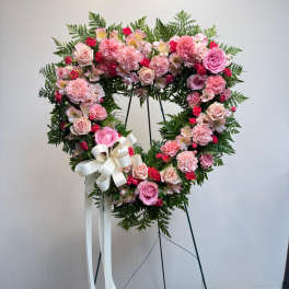 Heart-shaped pink floral wreath on a stand with a white ribbon bow