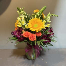 Mixed bouquet with orange roses, yellow daisies, and purple flowers in a glass vase