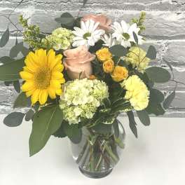 Mixed bouquet of yellow, pink, and white flowers in a glass vase