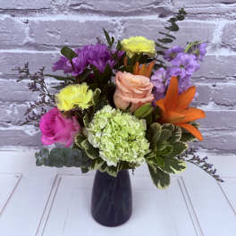 Mixed bouquet in a dark vase with roses, hydrangea, lilies, and purple blooms