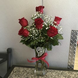 Red roses with baby's breath in a clear glass vase tied with a pink ribbon