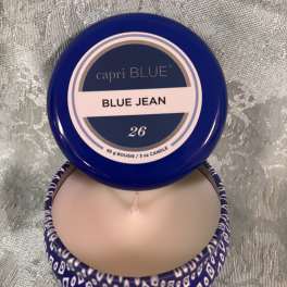 Blue-lidded candle tin labeled Blue Jean, shown open with a pale wax candle inside.
