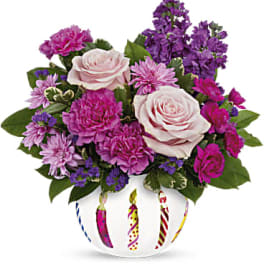 Pink and purple flower arrangement in a white vase with candle designs