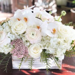 White floral arrangement in a rectangular wooden box with orchids and roses