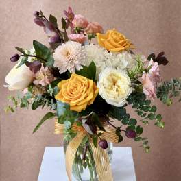 Bouquet of yellow, white, pink, and purple flowers in a glass vase with a ribbon