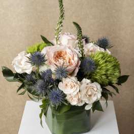Peach and white roses in a green glass vase with blue thistle and green pom-pom flowers