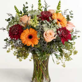 Mixed bouquet of orange gerbera daisies, peach roses, and burgundy mums in a glass vase