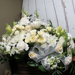 White floral arrangement with roses, daisies, and lilies in a basket
