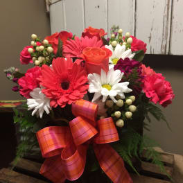 Bouquet of pink and orange flowers with a plaid ribbon in a dark container