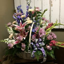 Basket arrangement with pink lilies, lavender roses, and blue flowers