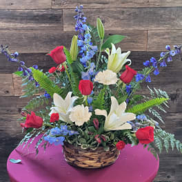 Basket arrangement with red roses, white lilies, and blue flowers