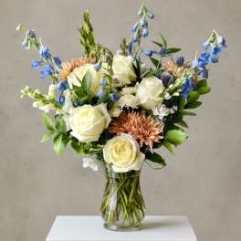Bouquet of white roses, blue flowers, and peach blooms in a clear glass vase