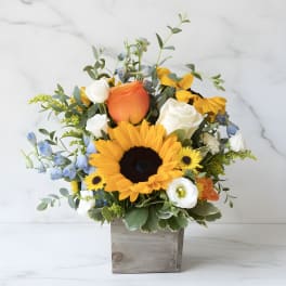 Sunflower bouquet with roses and blue flowers in a wooden box