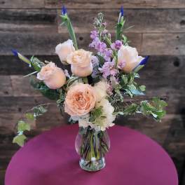 Peach roses and pink flowers in a clear glass vase