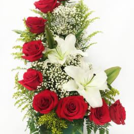 Tall arrangement of red roses and white lilies in a green glass vase with filler flowers.