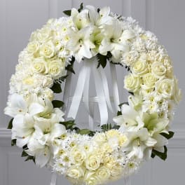 White floral wreath on a stand with roses and lilies