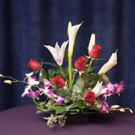 Arrangement of red roses, white calla lilies, and pink orchids in a black vase
