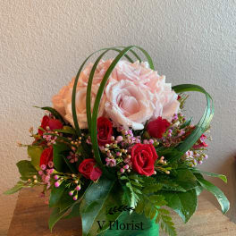 Short arrangement of pink and red roses with looping grass in a green cube vase