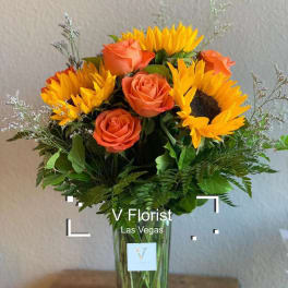 Tall vase of yellow sunflowers and orange roses in a clear glass rectangular vase.