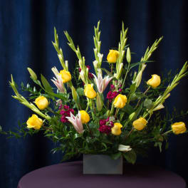 Yellow roses and lilies arranged in a square vase