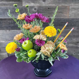 Mixed flower arrangement in a black vase with green apples and pencils
