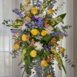 Tall floral spray with yellow roses, blue flowers, and white blooms on a stand