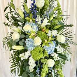 Tall floral spray with white roses, lilies, blue hydrangeas, and green blooms