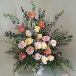 Tall bouquet of pastel roses in a white vase with purple accent flowers