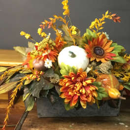 Autumn centerpiece with orange flowers, pumpkins, and a white gourd in a rectangular container