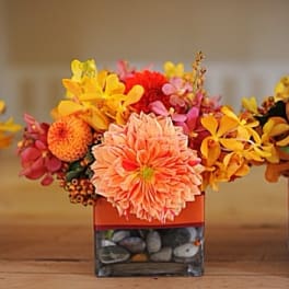 Orange and yellow floral arrangement in a square glass vase