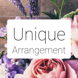 Pink rose and purple flowers behind a sign reading Unique Arrangement