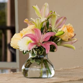 Pink lilies and pale roses arranged in a clear glass vase