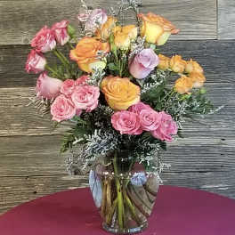 Arrangement of pink, orange, and yellow roses with white filler flowers in a clear glass vase.