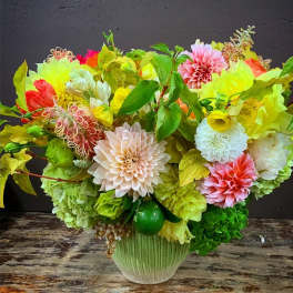 Bright mixed floral arrangement in a green vase with pink, yellow, white, and green blooms