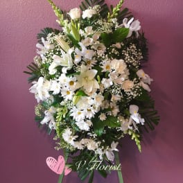 White floral standing spray with lilies and daisies on a purple wall