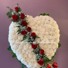 Heart-shaped white floral arrangement with red roses on a stand