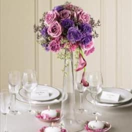 Tall centerpiece of pink and purple roses in a clear vase