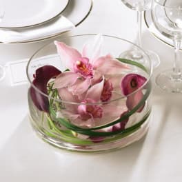Pink orchids arranged in a clear glass bowl on a table setting.