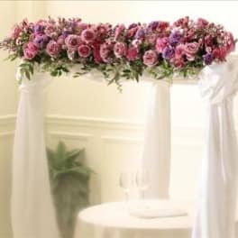 Pink and purple floral arrangement draped over a white arch