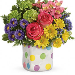 Colorful bouquet of roses, daisies, and purple flowers in a polka-dot vase