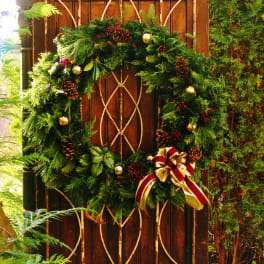 Evergreen wreath with pinecones and a red-and-gold bow on a wooden gate